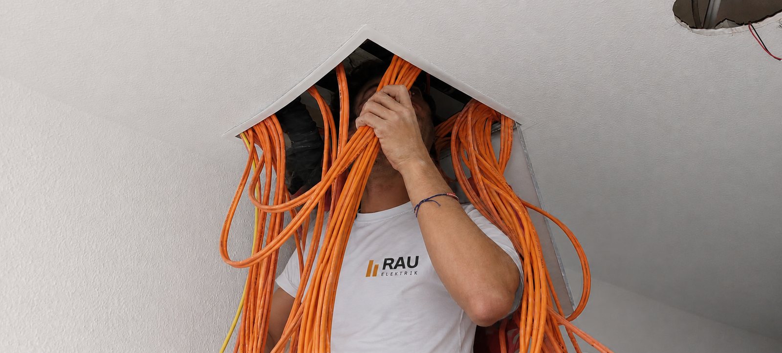 Julius Rau zieht orangefarbene Leitungen durch eine geöffnete Zwischendecke